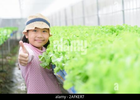 Carino ragazza asiatica che mostra il pollice fino al vegetale organico farm a Lop Buri, Thailandia. Cibo sano concetto Foto Stock