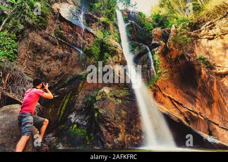 Fotografo viaggiatore fare foto incredibile cascata tropicale nascosta nella foresta pluviale. Viaggi stile di vita e di successo vacanze concetto nella natura selvaggia Foto Stock