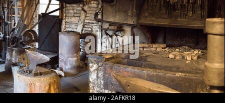 Una vista interna di una vecchia fucina di ferro e negozio di fabbro con incudine e fuoco e altre apparecchiature Foto Stock