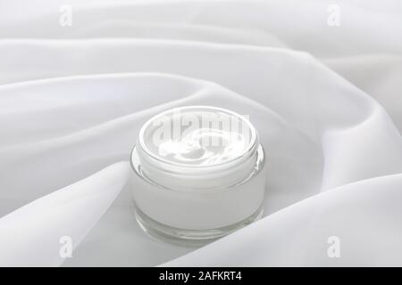 Vasetto di inverno la crema per la pelle sul tessuto bianco di sfondo, closeup. Spazio per il testo Foto Stock