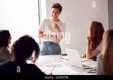 Femmina dà risalto alla presentazione ai team di giovani imprenditrici riuniti intorno al tavolo in ufficio moderno Foto Stock