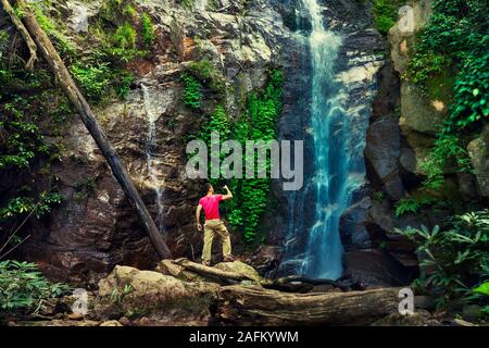 Fotografo viaggiatore fare foto incredibile cascata tropicale nascosta nella foresta pluviale. Viaggi stile di vita e di successo vacanze concetto nella natura selvaggia Foto Stock