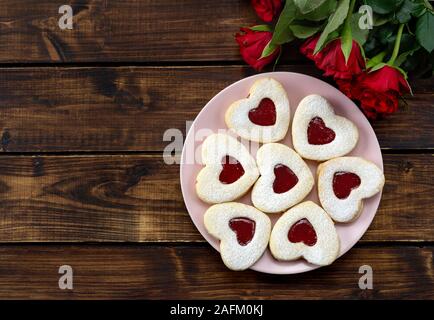 Close up a forma di cuore ad Linzer cookies nella piastra di rosa sul tavolo di legno Foto Stock