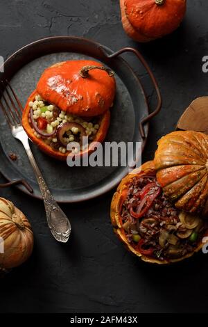 Sano cibo vegan. Piccolo arancione zucca ripieni di riso rosso, funghi, porro, peperone, couscous gigante e uvetta su vintage vassoio metallico sul nero b Foto Stock