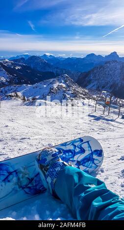 Uno snowboarder prendendo una pausa sul pendio. Lo snowboard è bianco e blu, armoniosamente il raccordo per la natura condizioni - il bianco della neve e il blu del cielo. T Foto Stock