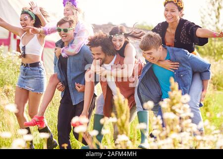 Gruppo di amici a piedi Torna alla tenda dopo aver aperto il Festival di musica con gli uomini che le donne piggyback Foto Stock