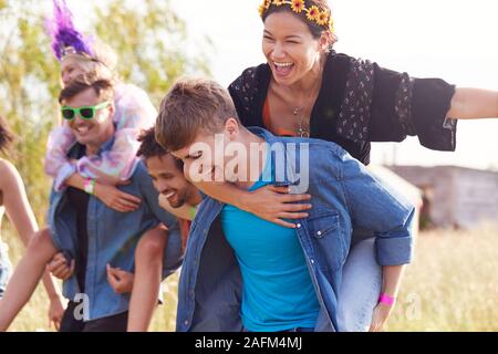 Gruppo di amici a piedi Torna alla tenda dopo aver aperto il Festival di musica con gli uomini che le donne piggyback Foto Stock