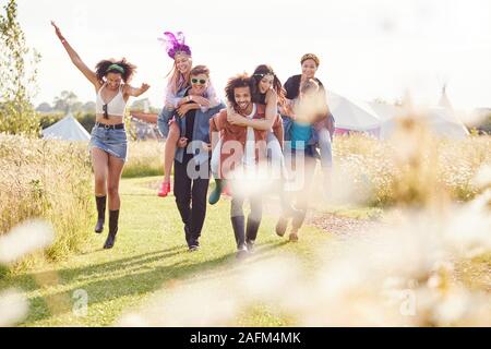 Gruppo di amici a piedi Torna alla tenda dopo aver aperto il Festival di musica con gli uomini che le donne piggyback Foto Stock