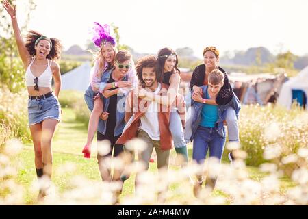 Gruppo di amici a piedi Torna alla tenda dopo aver aperto il Festival di musica con gli uomini che le donne piggyback Foto Stock