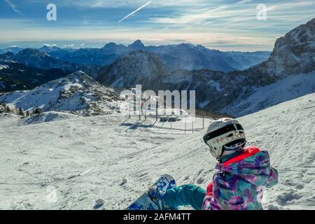 Uno snowboarder prendendo una pausa sul pendio. Lo snowboard è bianco e blu, armoniosamente il raccordo per la natura condizioni - il bianco della neve e il blu del cielo. T Foto Stock