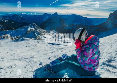 Uno snowboarder prendendo una pausa sul pendio. Lo snowboard è bianco e blu, armoniosamente il raccordo per la natura condizioni - il bianco della neve e il blu del cielo. T Foto Stock