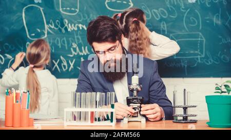 Uomo Barbuto maestro lavora con microscopio e provette per la prova in biologia classe. Spiegare la biologia per i bambini. Biologia svolge ruolo nella comprensione delle complesse forme di vita. Insegnante della Scuola di biologia. Foto Stock