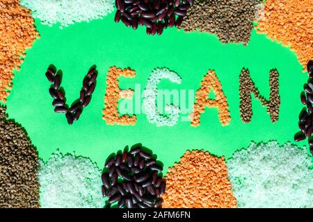 Telaio di diversi cereali con parola vegano su sfondo verde. Vegan parola fatta di grano vari. Mix di cereali e fagioli. Cibo vegetariano. Foto Stock