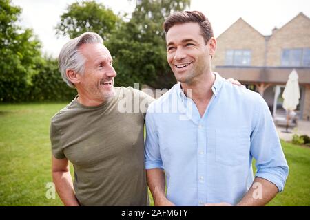 Senior padre e figlio adulto camminare e parlare in giardino insieme Foto Stock