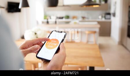 Close up uomo utilizzando App su Smart Phone alla centrale di controllo di temperatura di riscaldamento in casa Foto Stock
