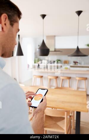 Uomo che utilizza App su Smart Phone alla centrale di controllo di temperatura di riscaldamento in casa Foto Stock