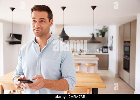 Uomo che utilizza App su Smart Phone alla centrale di controllo di temperatura di riscaldamento in casa Foto Stock