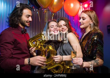 Due giovani donne sorridenti tintinnio flauti di champagne con eleganti uomo a parte Foto Stock