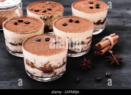 Tiramisù classico dessert in un vetro cosparso di cacao e decorate con i chicchi di caffè su uno sfondo scuro, dessert di lusso Foto Stock