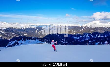 Uno snowboarder andando giù il pendio in Turrach, Austria. Piste perfettamente preparate. Le alte montagne che circondano la donna che indossa pantaloni rosa e colore Foto Stock