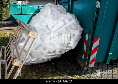 Il verde di contenitori per rifiuti riciclabili, un grande trasparente grande sacco di plastica con polistirolo e una tavolozza di legno appoggiata contro il sacco Foto Stock