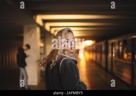 Giovane donna guardando indietro alla fotocamera camminando sulla stazione metropolitana Foto Stock