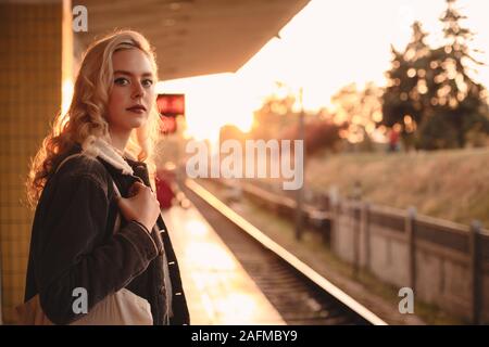 Giovane donna in attesa del treno alla stazione della metropolitana durante il tramonto Foto Stock