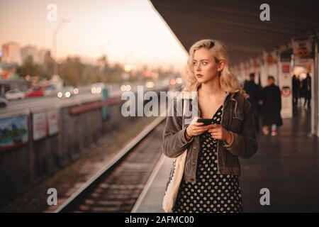 Giovane donna pensosa utilizzando smart phone durante l'attesa per il treno Foto Stock