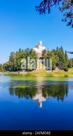 Una vista sul castello di Trakoscan dal lato lago. Il castello è situato su di una piccola collina e ben nascosto tra gli alberi. Il lago di fronte al castello Foto Stock