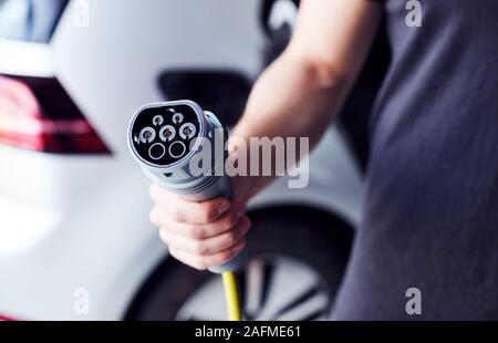 Stretta di mano che tiene il cavo di alimentazione per ecocompatibili Emissioni Zero auto elettrica Foto Stock