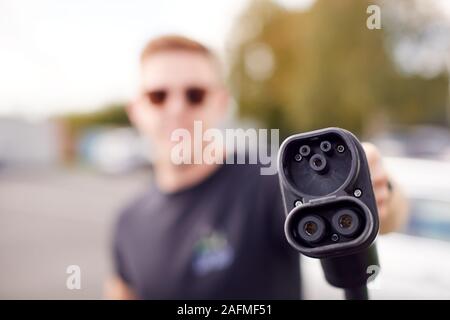 L'uomo potere di tenuta cavo di ricarica per auto elettrica nel parcheggio auto esterno Foto Stock