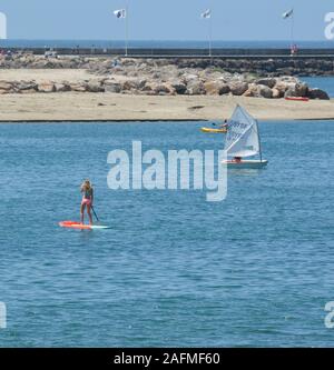 Vista posteriore della donna bionda in bikini su SUPB con altri ricreando con sport d'acqua vicino al molo del porto di Santa Barbara in California Foto Stock