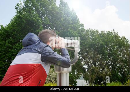 Giovane uomo guardando attraverso il telescopio per il panorama del paesaggio nella giornata di sole. Hipster ragazzo indossa abiti casual gode di rilassarsi in un fine settimana estivo Foto Stock