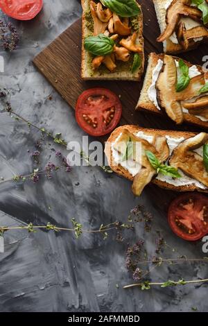 Sani snack vegetariano. Bruschette con chanterelle e funghi porcini con pomodoro e basilico foglie su sfondo scuro vista dall'alto uno spazio di copia Foto Stock