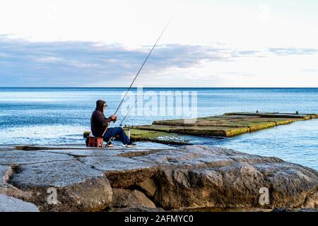 Un pescatore solitario con una canna da pesca si siede su una roccia dal mare. Vacanze attive sul Mar Nero. Foto Stock