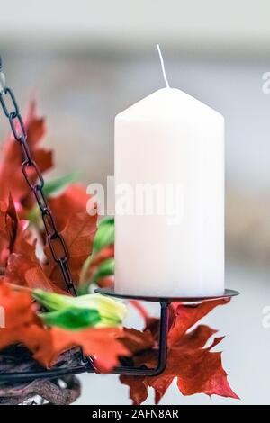 Frammento di una corona di Avvento appeso su catene. Uno non illuminata candela bianco e la decorazione di foglie rosse e fiori di colore giallo. Foto Stock