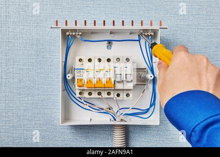Il programma di installazione installa una apparecchiatura di interruzione e sezionamento elettrico in casa. Montaggio della scatola dei fusibili all'interno di un armadio elettrico, l'elettricista si stringe la vite di io Foto Stock