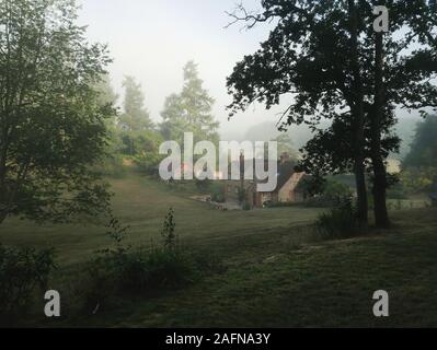 La quintessenza Inglese cottage di campagna in misty valle circondata da alberi Foto Stock