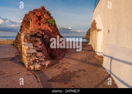 Un red rock e un muro di casa con il mare e le nuvole in background, visto in Babbacombe Beach, Torbay, England, Regno Unito Foto Stock