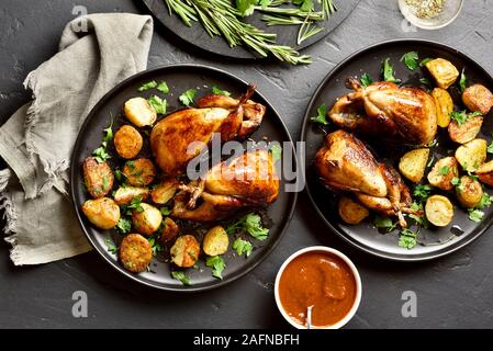 Quaglie arrosto carcasse con patate su lastra in pietra nera dello sfondo. Gustoso quaglie fritto con verdure. Vista superiore, laici piatta Foto Stock