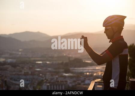 Ciclista di scattare una foto con Smart Phone. Viaggiatore fare foto su smartphone utilizzando il telefono in mano, viaggio Blogger. Uomo sportivo con bicicletta utilizzare il telefono Foto Stock