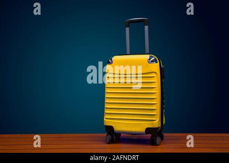 Colore giallo valigia viaggio su sfondo scuro con spazio di copia Foto Stock