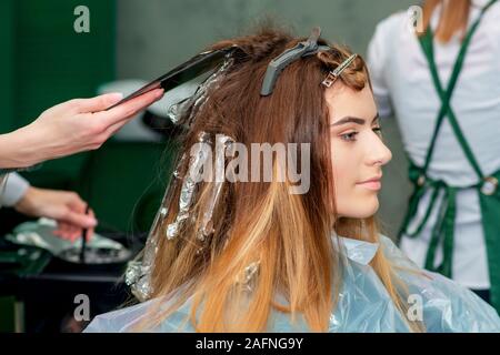 Giovane donna la ricezione di tingere i capelli dal parrucchiere in salotto. Foto Stock