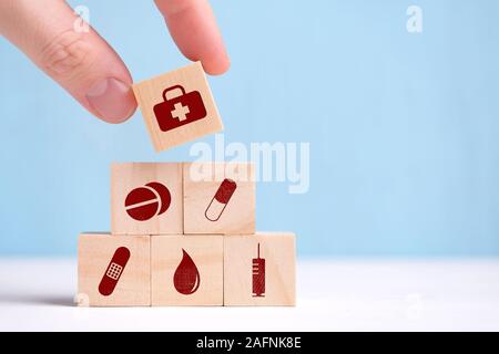 La mano trattiene un cubo di legno con icone - compresse, capsule, Band-Aid, prove, siringa. Close up. Foto Stock