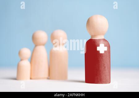 Il concetto di un medico di famiglia accanto a una coppia di sposi e di un bambino. Statuine di legno su uno sfondo blu. Close up. Foto Stock