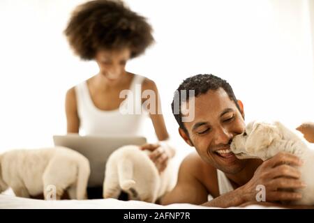 L'uomo gioca con i cuccioli mentre la ragazza guarda allo schermo di un notebook. Foto Stock