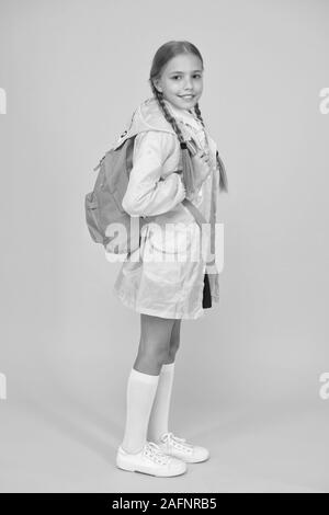 Sulla schiena e pronto ad andare a scuola. Piccola scuola ragazza carina usura impermeabile su sfondo giallo. Adorable kid con la scuola zaino sul giorno di pioggia. Un bambino piccolo si torna a scuola in autunno. Foto Stock