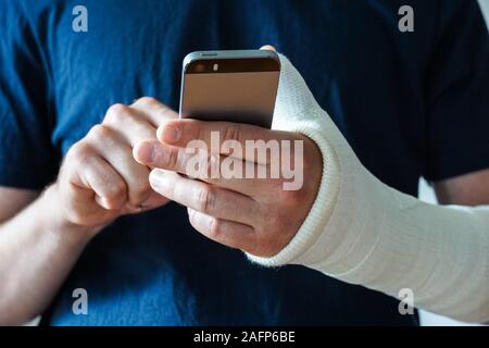 Uomo con il calco in gesso sulla mano rotti, rotto il pollice,polso rotto utilizza lo smartphone Foto Stock