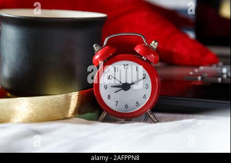 Close up sveglia rossa, il computer laptop e la tazza di caffè nel letto. Area di lavoro per freelance. Ora di scadenza del concetto. Lay piatto Foto Stock