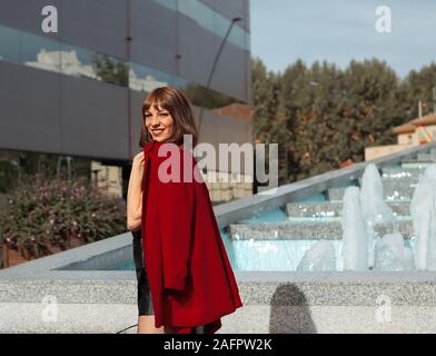 Bella giovane donna con giacca rossa sorridente e godendo della città Foto Stock